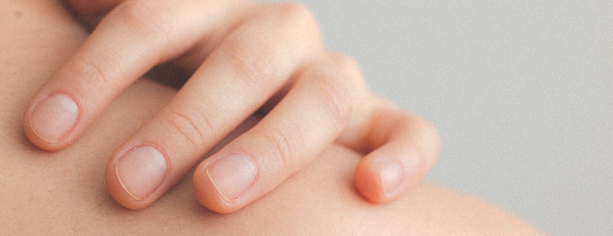 Mano delicadamente apoyada sobre un hombro, mostrando una piel suave y tonos neutros de fondo.