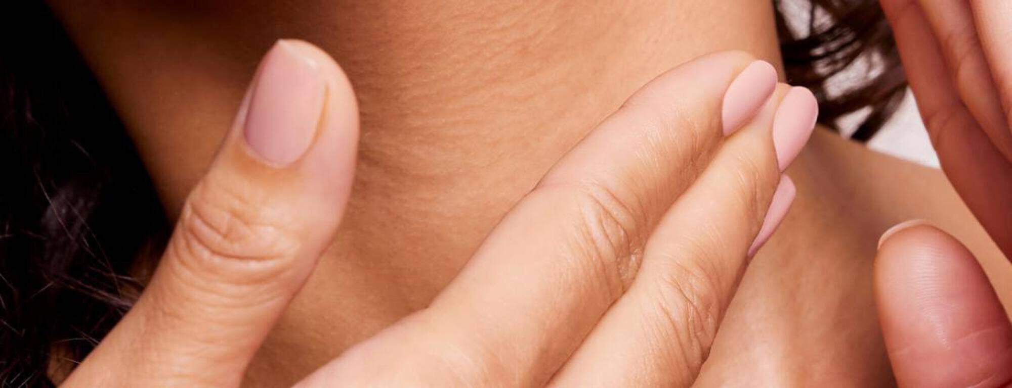 Manos aplicando crema en el cuello de una persona, destacando la piel suave y bien cuidada.