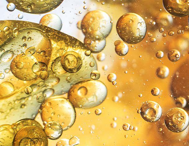 Close-up of bubbles in liquid, showcasing a mix of gold and amber tones with light reflections creating an abstract effect.
