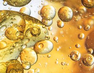 Close-up of bubbles in liquid, showcasing a mix of gold and amber tones with light reflections creating an abstract effect.