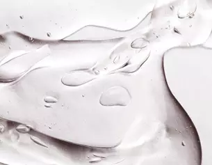 Texto en espanol: 'Gotas de agua y gel sobre una superficie blanca, creando un efecto de transparencia y suavidad.'