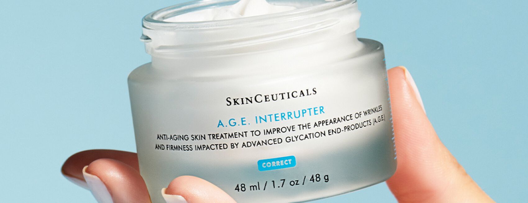 Frasco de crema antienvejecimiento A.G.E. Interrupter de SkinCeuticals, en una mano, sobre fondo azul claro.