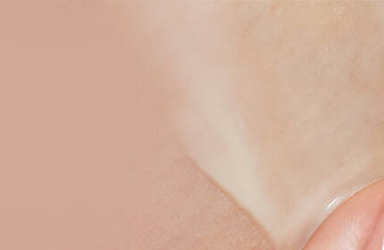 A close-up of a hand applying a translucent skincare product to the skin, highlighting the smooth texture against a soft, neutral background.