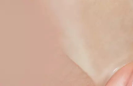 A close-up of a hand applying a translucent skincare product to the skin, highlighting the smooth texture against a soft, neutral background.