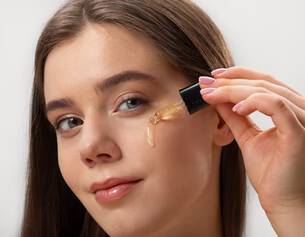 Mujer aplicando un suero facial con cuentagotas sobre su piel, luciendo un rostro fresco y luminoso.