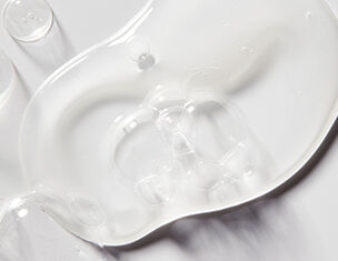Clear gel or liquid spilled on a smooth white surface, showcasing a glossy texture and light reflections.