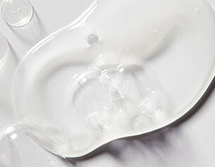 Clear gel or liquid spilled on a smooth white surface, showcasing a glossy texture and light reflections.