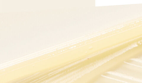 A close-up of a smooth, creamy texture resembling butter against a light, neutral background.