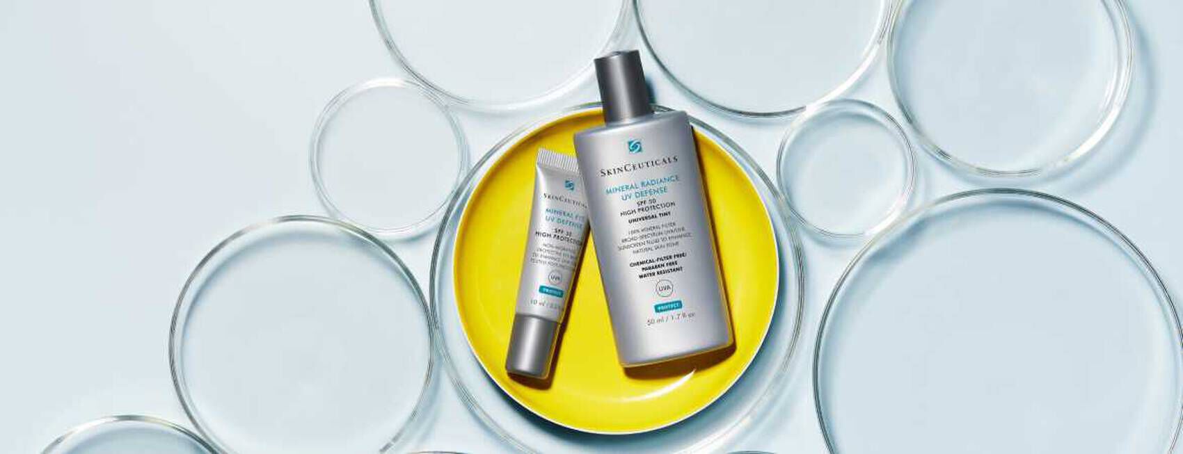 Productos de cuidado facial de SkinCeuticals sobre un fondo de burbujas de agua en tonos suaves.