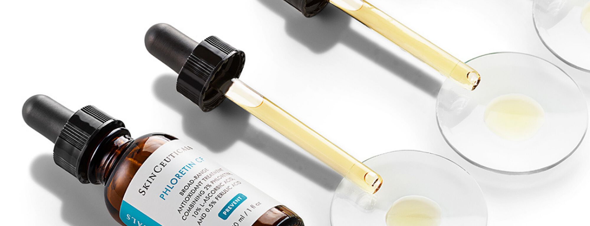Botellas de suero Skinceuticals con goteros y muestras en platos, destacando su color y textura.
