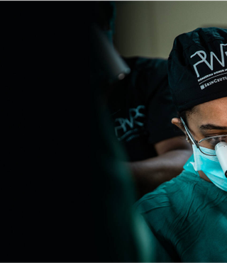 Un cirujano concentrado, usando mascarilla y lupa, en un entorno quirurgico.