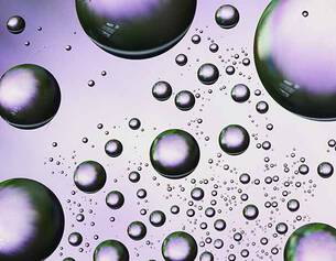 Close-up of iridescent bubbles in various sizes, reflecting light against a soft purple background.