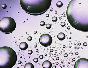 Close-up of iridescent bubbles in various sizes, reflecting light against a soft purple background.