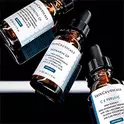 Tres frascos de serum con Vitamina C de SkinCeuticals, sobre un fondo oscuro y reflectante.