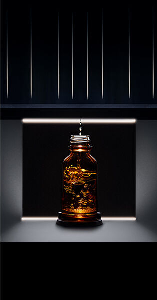 Botella de vidrio oscura con un liquido dorado iluminada suavemente en un entorno oscuro.