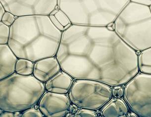 Primer plano de burbujas de jabon, mostrando estructuras hexagonales y la luz reflejada en una superficie suave.