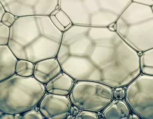 Primer plano de burbujas de jabon, mostrando estructuras hexagonales y la luz reflejada en una superficie suave.