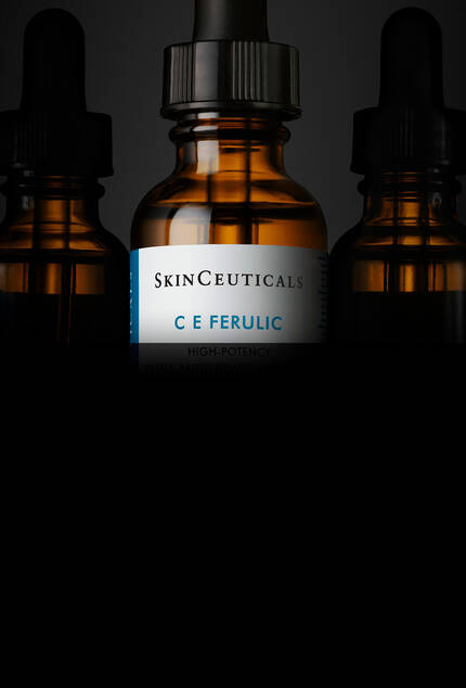 Botellas de suero de SkinCeuticals con etiquetas visibles, destacando el producto "C E Ferulic", sobre un fondo oscuro.