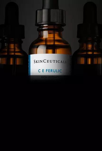 Botellas de suero de SkinCeuticals con etiquetas visibles, destacando el producto "C E Ferulic", sobre un fondo oscuro.