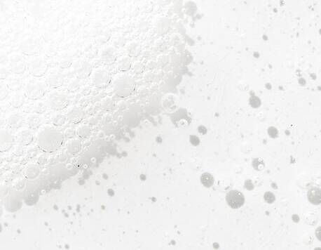 Close-up of white foam with varying bubble sizes against a light background, creating a textured, ethereal effect.