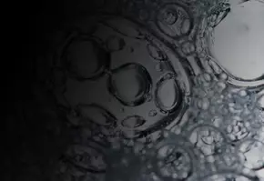 Close-up of bubbles in dark liquid, showcasing intricate shapes and reflections of light.