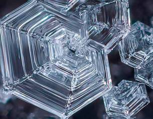 Close-up of intricate, shining ice crystals with a geometric, hexagonal structure against a dark background.
