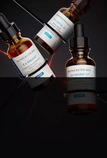 Tres botellas de suero, con etiquetas de "SkinCeuticals", sobre un fondo oscuro. Una de las botellas esta inclinada, mientras que las otras dos estan en posicion vertical.
