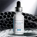 Un frasco de serum Discoloration Defense de SkinCeuticals sobre una superficie reflectante, contra un fondo oscuro y texturizado.