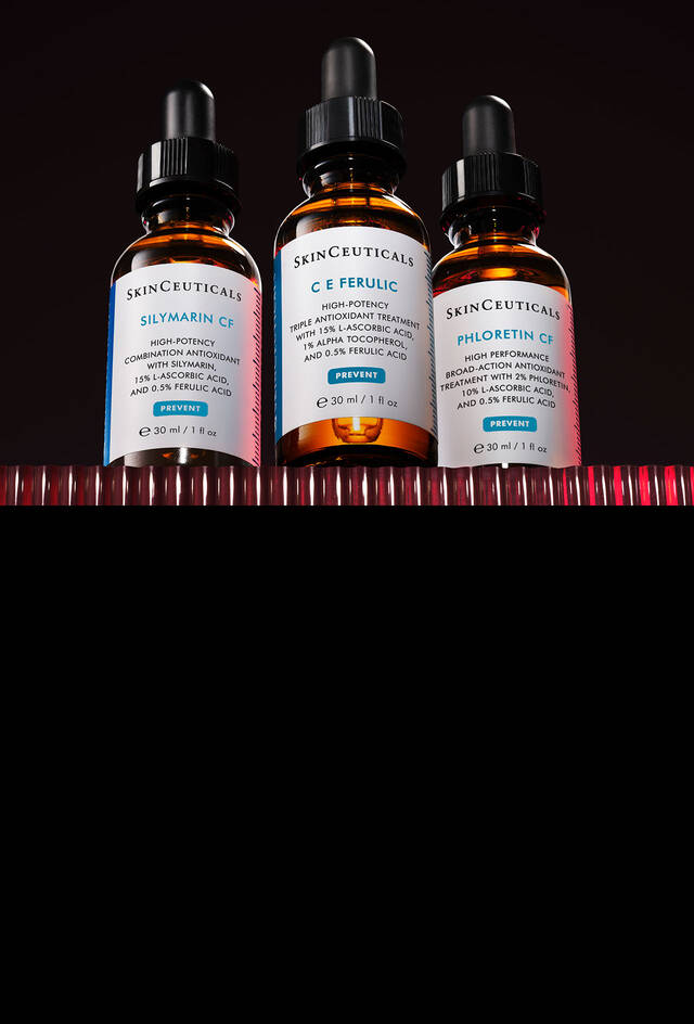 Una caja de regalo transparente atada con una cinta dorada, que contiene productos de SkinCeuticals: dos frascos de serum (CE Ferulic y P-Tiox) y un tarro de Triple Lipid Restore 2:4:2