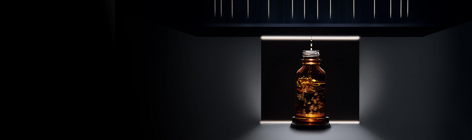 Botella de vidrio ambar iluminada desde abajo, situada en un entorno oscuro con detalles arquitectonicos en el fondo.