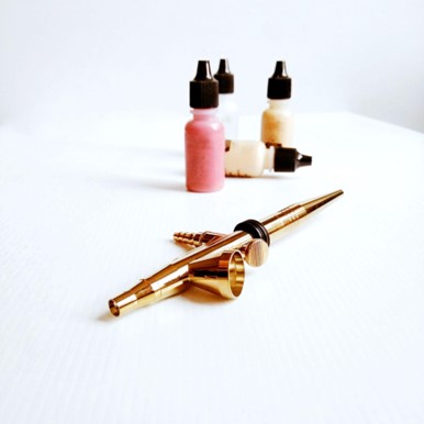Un bolígrafo dorado y botellas de tinta en colores, sobre una superficie blanca, ideal para arte o diseño.