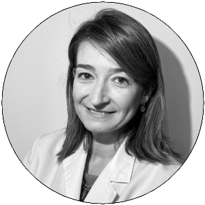 Retrato en blanco y negro de una mujer con cabello castaño, sonriendo y vestida con una chaqueta clara.
