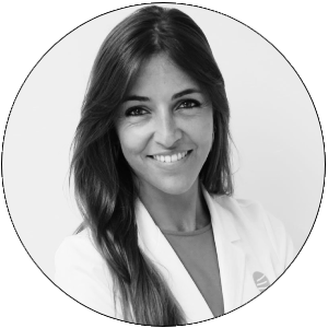 Una mujer sonriente con cabello largo y lacio, vestida con una chaqueta blanca de laboratorio.