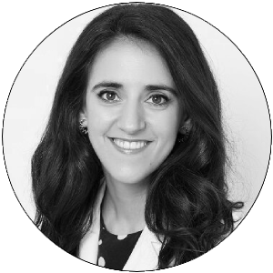 Retrato en blanco y negro de una mujer con cabello largo y oscuro, sonriendo, vestida con una chaqueta blanca.